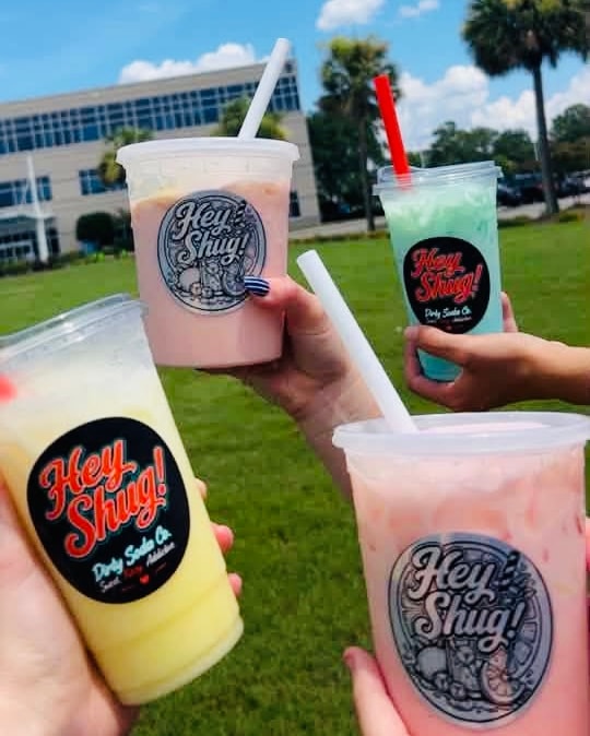 Hey Shug! cups held up at an outdoor event
